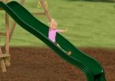 Little girl sliding down a green Giant Scoop Wave Slide on a backyard playset